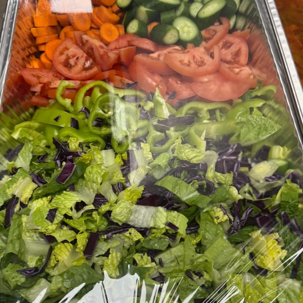 A foil tray filled with fresh salad ingredients, including lettuce, bell peppers, tomatoes, carrots, and cucumbers.