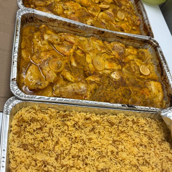 Three foil trays of food, two with lemon-garnished fish in sauce and one with rice.