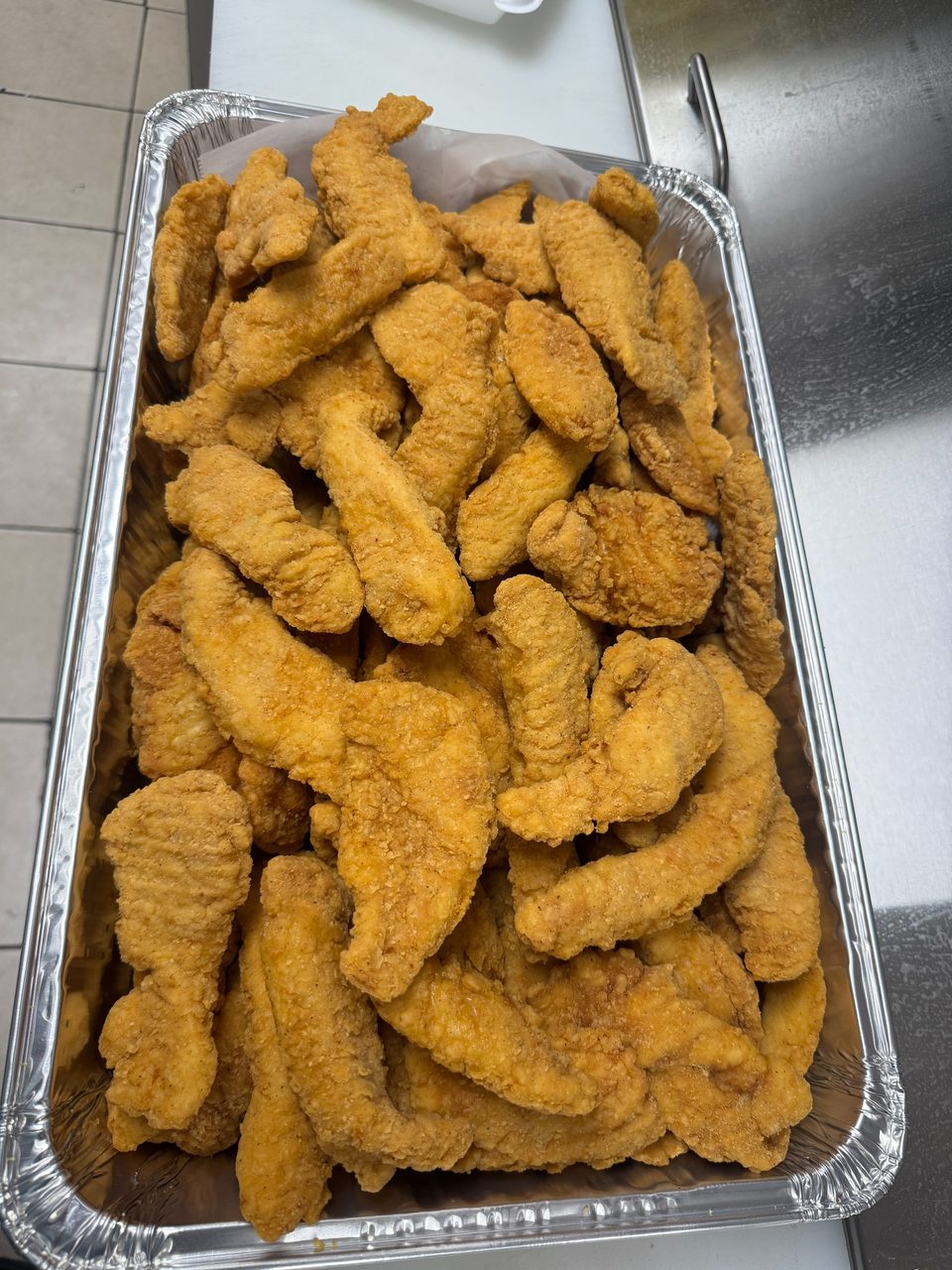 A large aluminum tray filled with golden-brown, crispy fried chicken tenders.