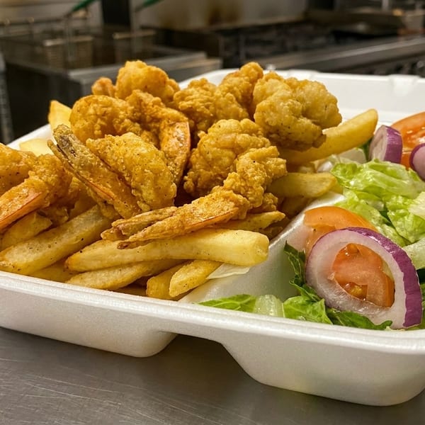 Fried shrimp and french fries with a side salad in a white takeout container.