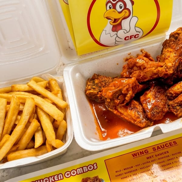 CFC hot wings with sauce and a side of fries in white takeout containers.