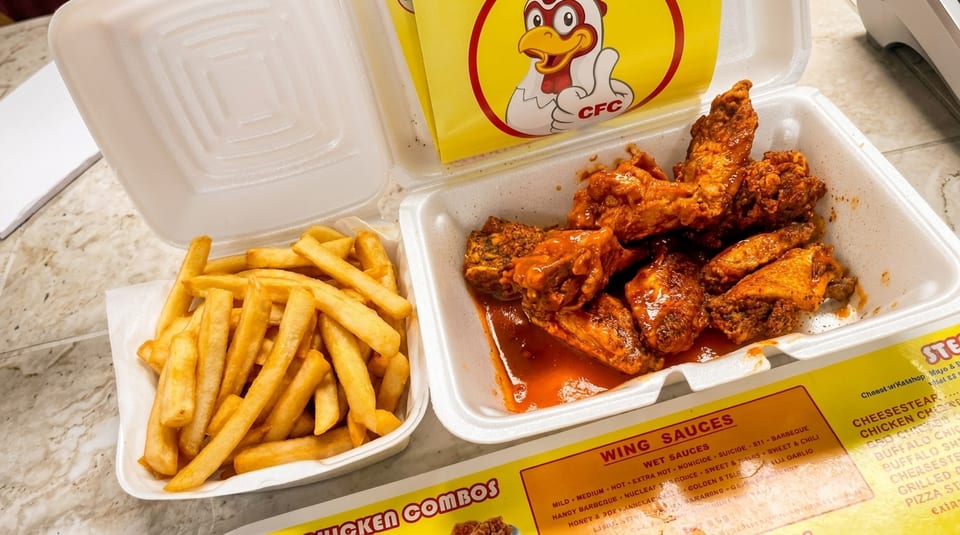 CFC hot wings with sauce and a side of fries in white takeout containers.