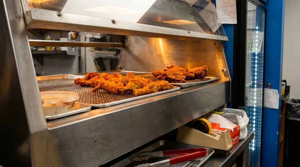 Crispy fried chicken pieces on metal trays under a warming lamp in a restaurant kitchen.