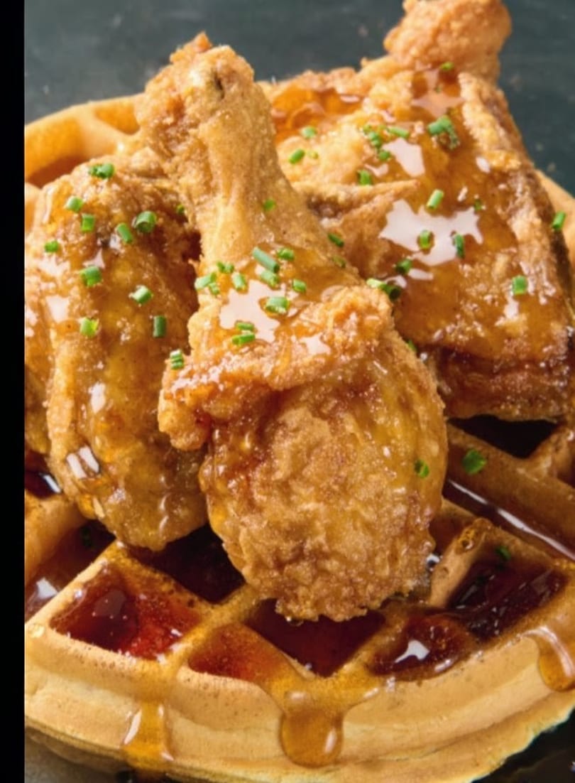Crispy fried chicken drumsticks and wings drizzled with syrup and chives, served on a golden waffle.