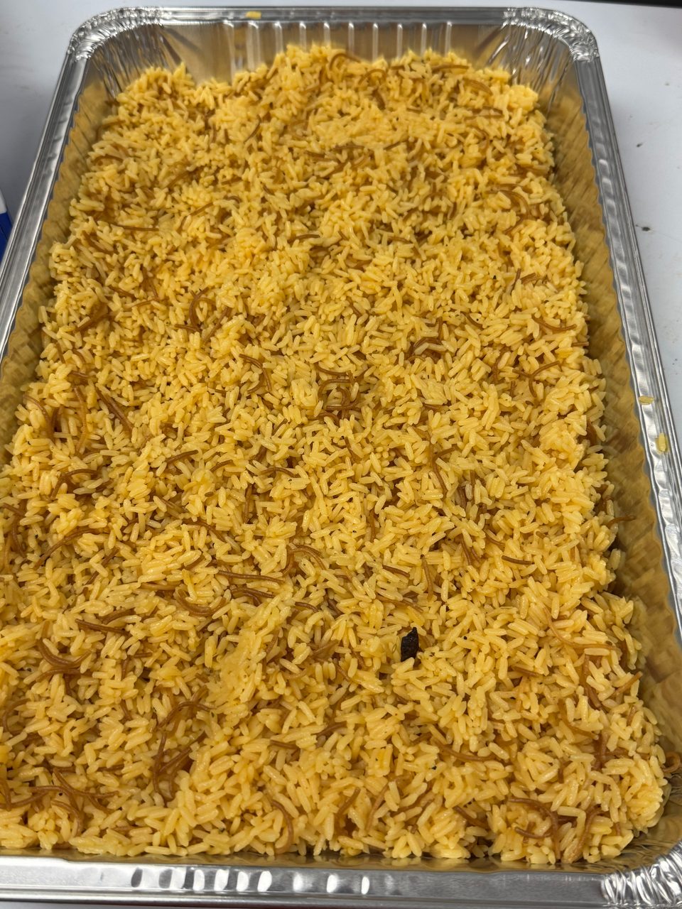A large aluminum tray filled with yellow rice and vermicelli noodles, ready for serving.