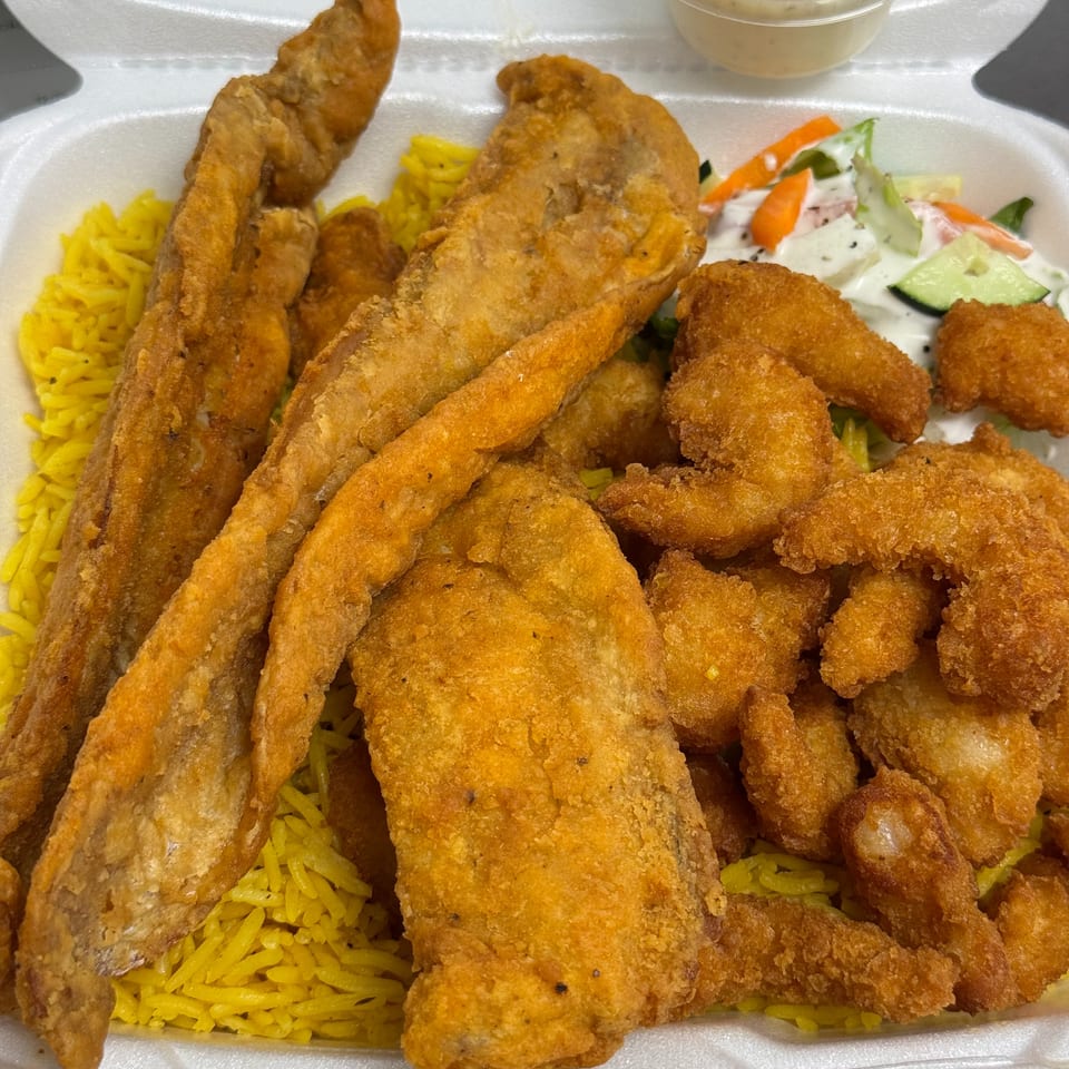 Fried fish fillets and shrimp with yellow rice, salad, and tartar sauce in a takeout container.