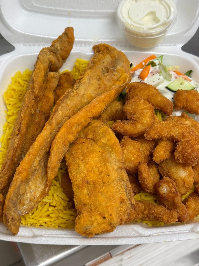 Fried fish fillets and shrimp with yellow rice, salad, and tartar sauce in a takeout container.